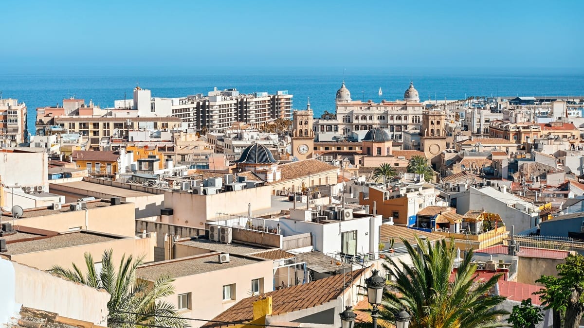Blick über die Dächer der Altstadt von Alicante mit Kirchtürmen und Kuppeln, dahinter das Mittelmeer