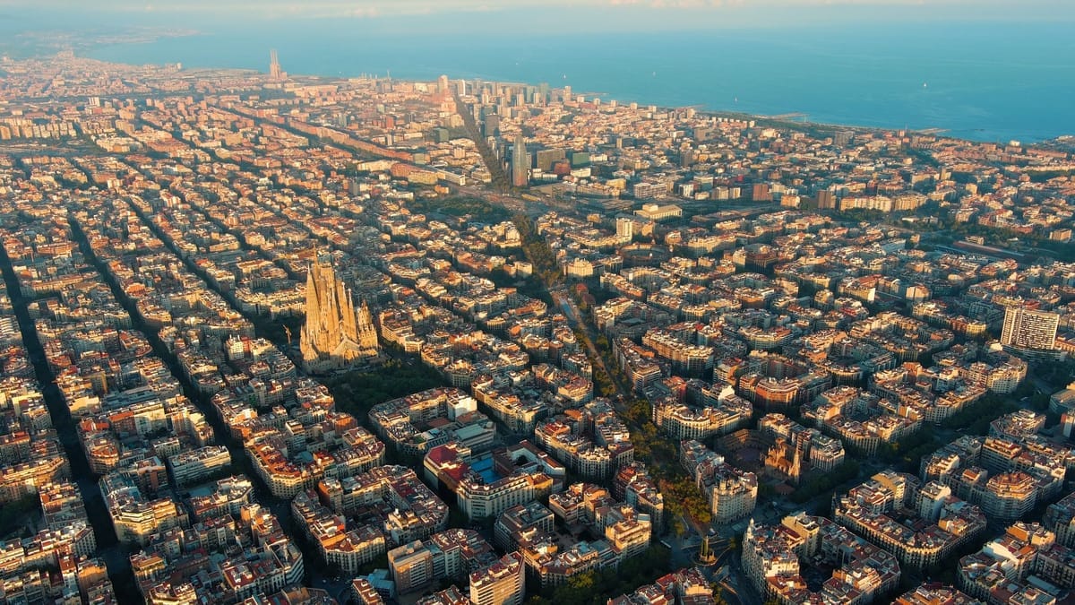 Luftaufnahme des Eixample-Rasters von Barcelona mit der Sagrada Família links und dem Mittelmeer im Hintergrund