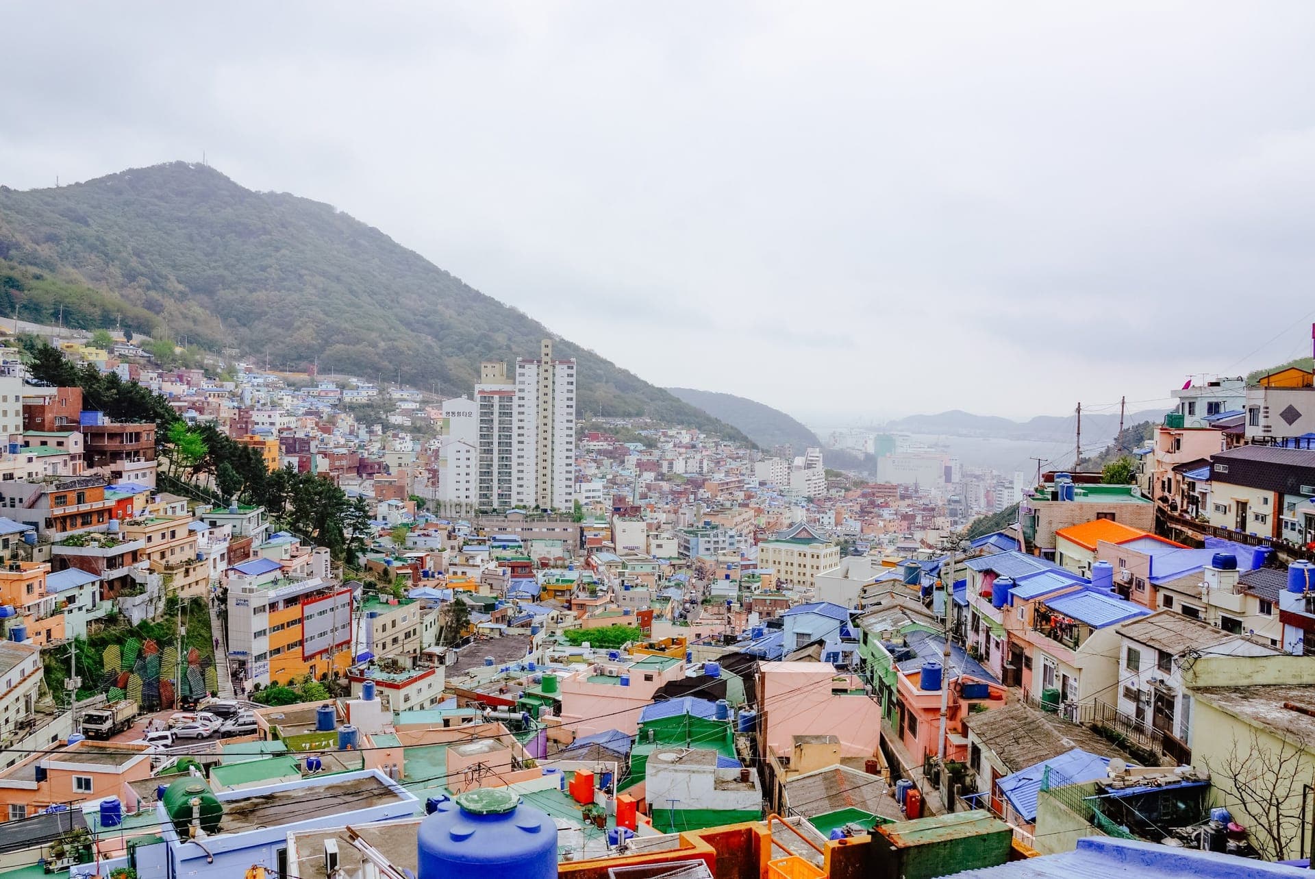 Blick über die bunten, terrassenförmig gebauten Häuser des Gamcheon-Kulturdorfs in Busan mit dem Meer im Hintergrund