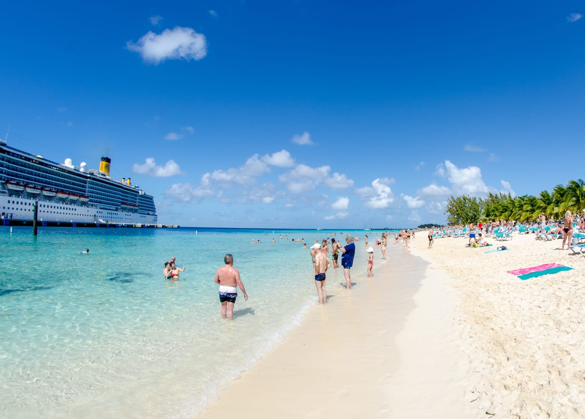 Tropischer Strand auf Grand Cayman mit türkisfarbenem Wasser, Badegästen und einem Kreuzfahrtschiff auf Reede dahinter