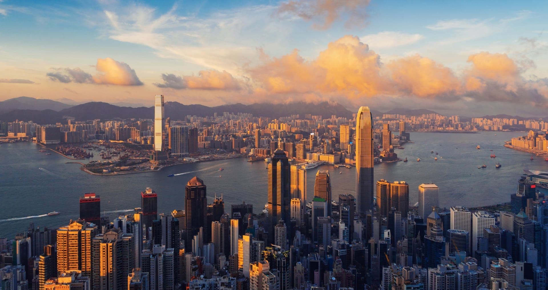 Blick von oben über die Hochhäuser von Hongkong Island und den Victoria Harbour im Abendlicht, dahinter die Halbinsel Kowloon