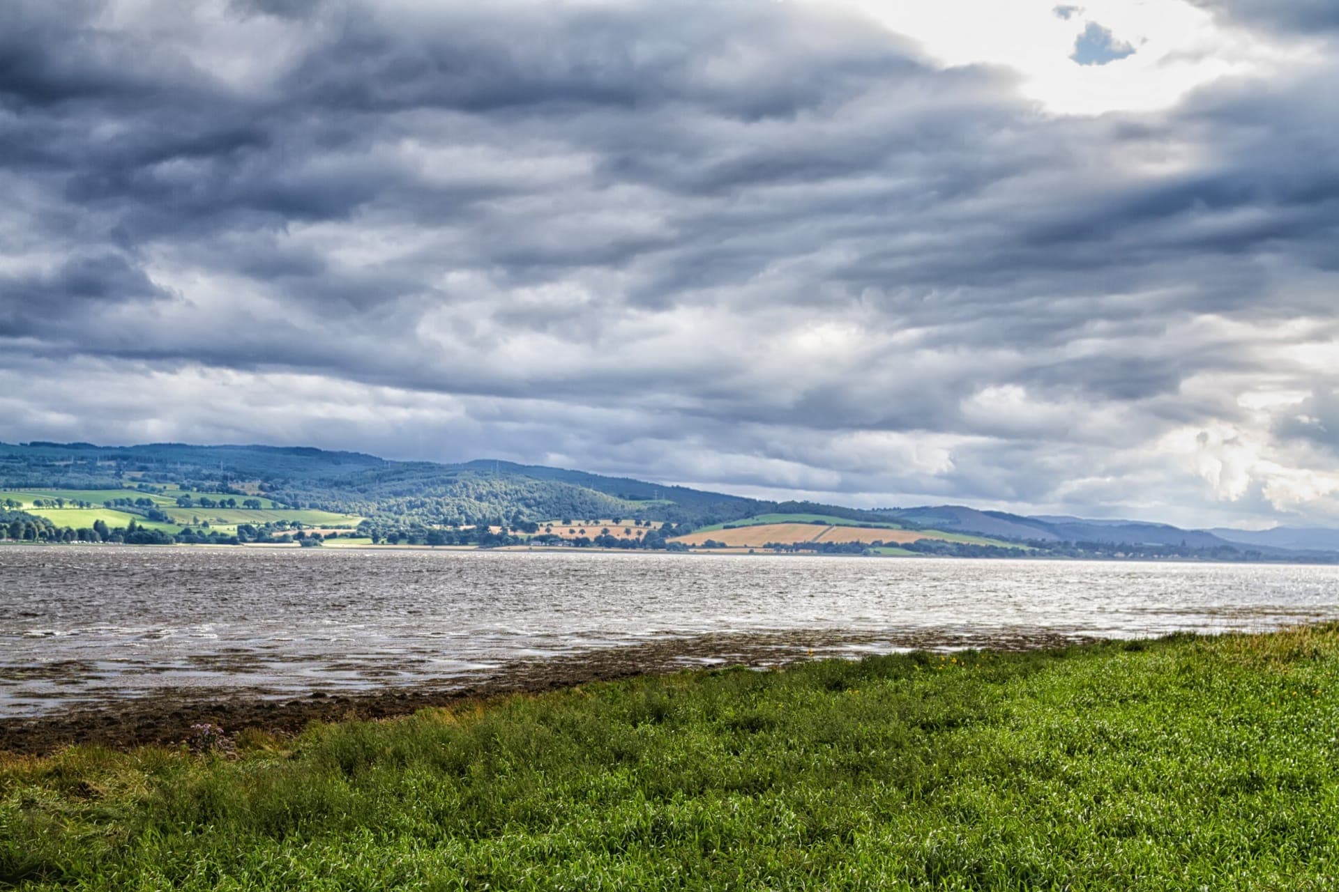 Der Cromarty Firth bei Invergordon mit grünen Hügeln der schottischen Highlands unter dramatischem Wolkenhimmel
