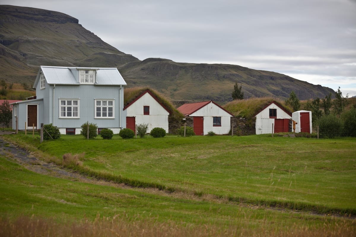 Traditionelle isländische Holzhäuser mit Grasdächern vor einer Bergkulisse in Westisland