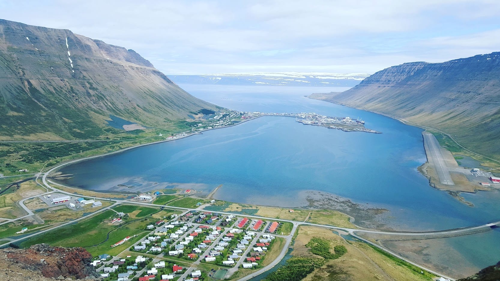 Blick von oben auf die Landzunge von Ísafjörður mit Hafen und Flugpiste im Skutulsfjörður, umgeben von steilen Tafelbergen der Westfjorde