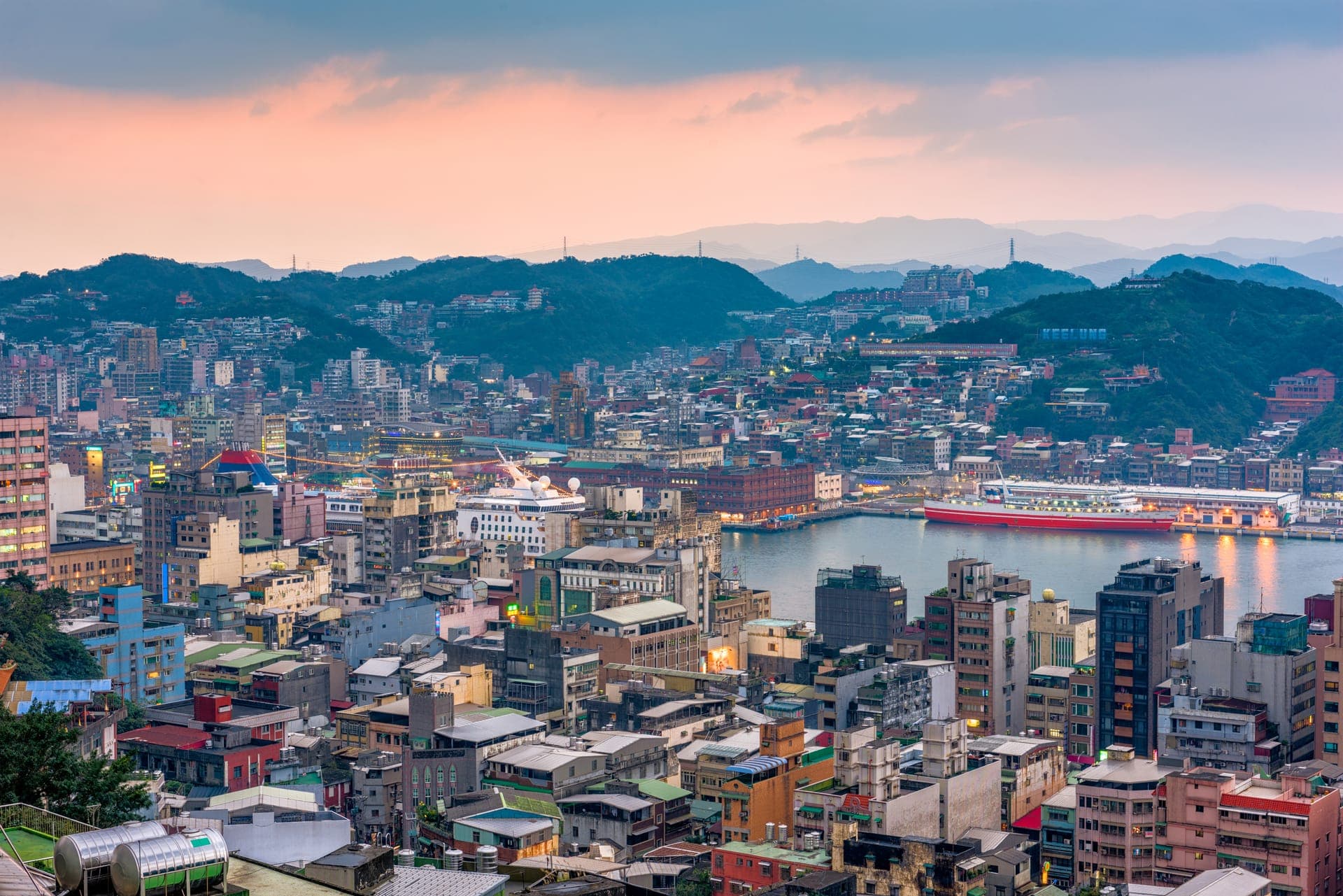 Luftbild der dicht bebauten Stadt Keelung in Taiwan zwischen bewaldeten Bergen im Abendlicht