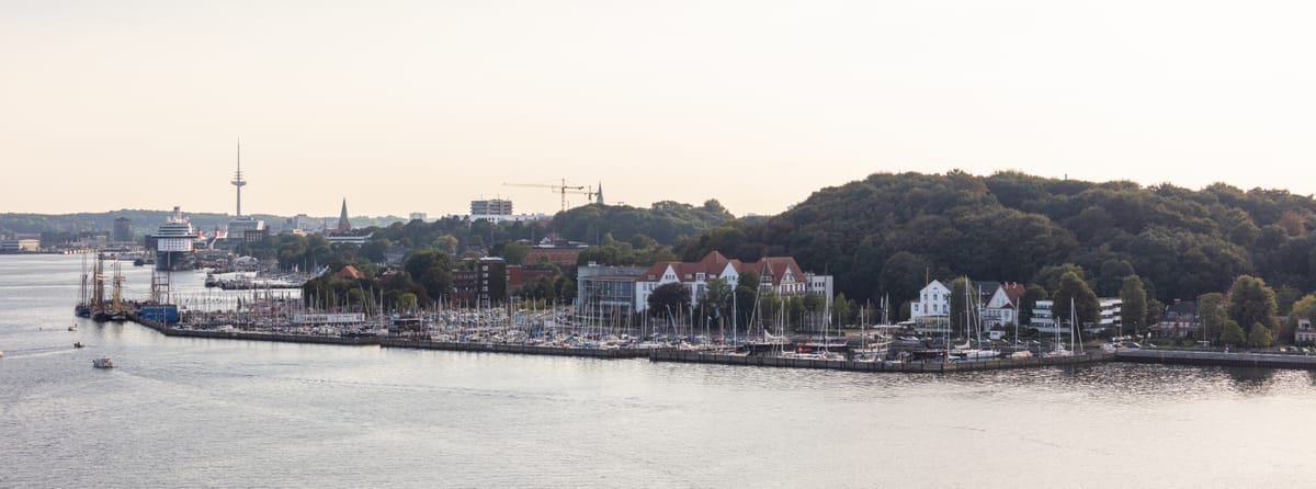 Die Kiellinie-Promenade an der Kieler Förde im Abendlicht, davor Segelboote am Ufer