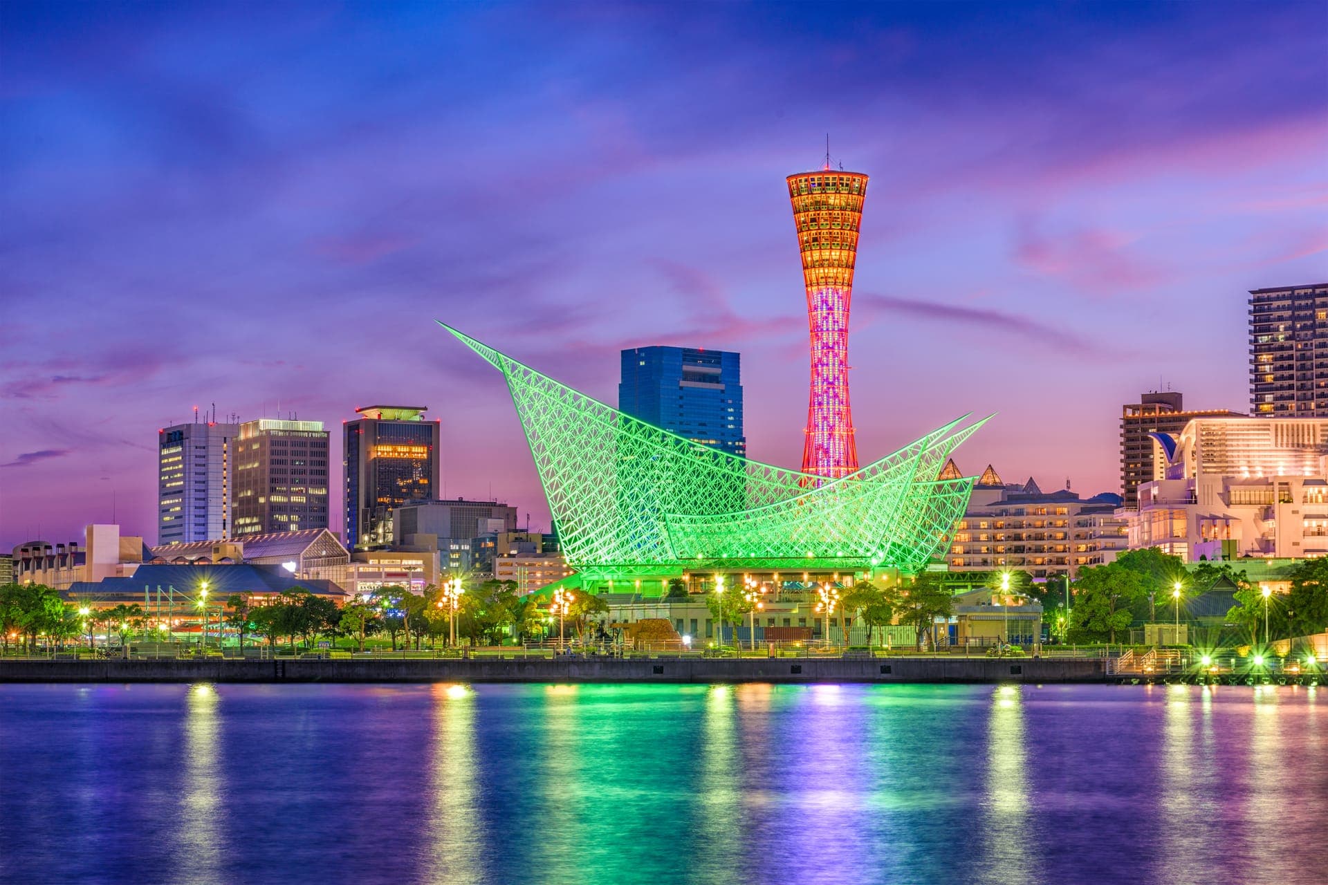 Der rot beleuchtete Kobe Port Tower und das grün leuchtende Maritime Museum spiegeln sich in der Abenddämmerung im Hafenbecken von Kobe