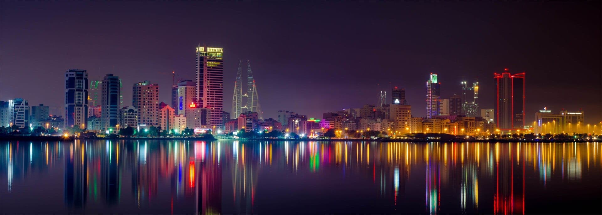 Die beleuchtete Skyline von Manama bei Nacht, die Hochhäuser spiegeln sich in der ruhigen Bucht