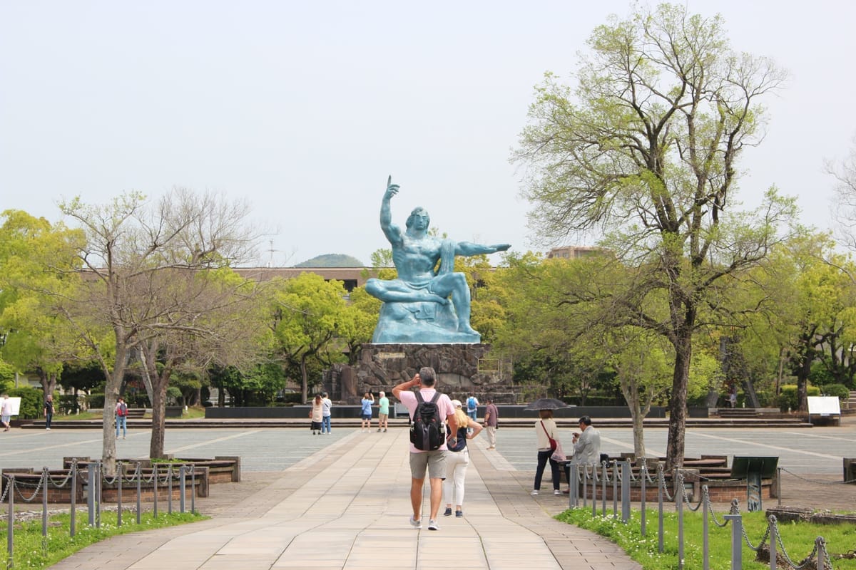 Die blaugrüne Friedensstatue am Ende der Parkachse im Friedenspark von Nagasaki, davor Besucher auf dem breiten Weg