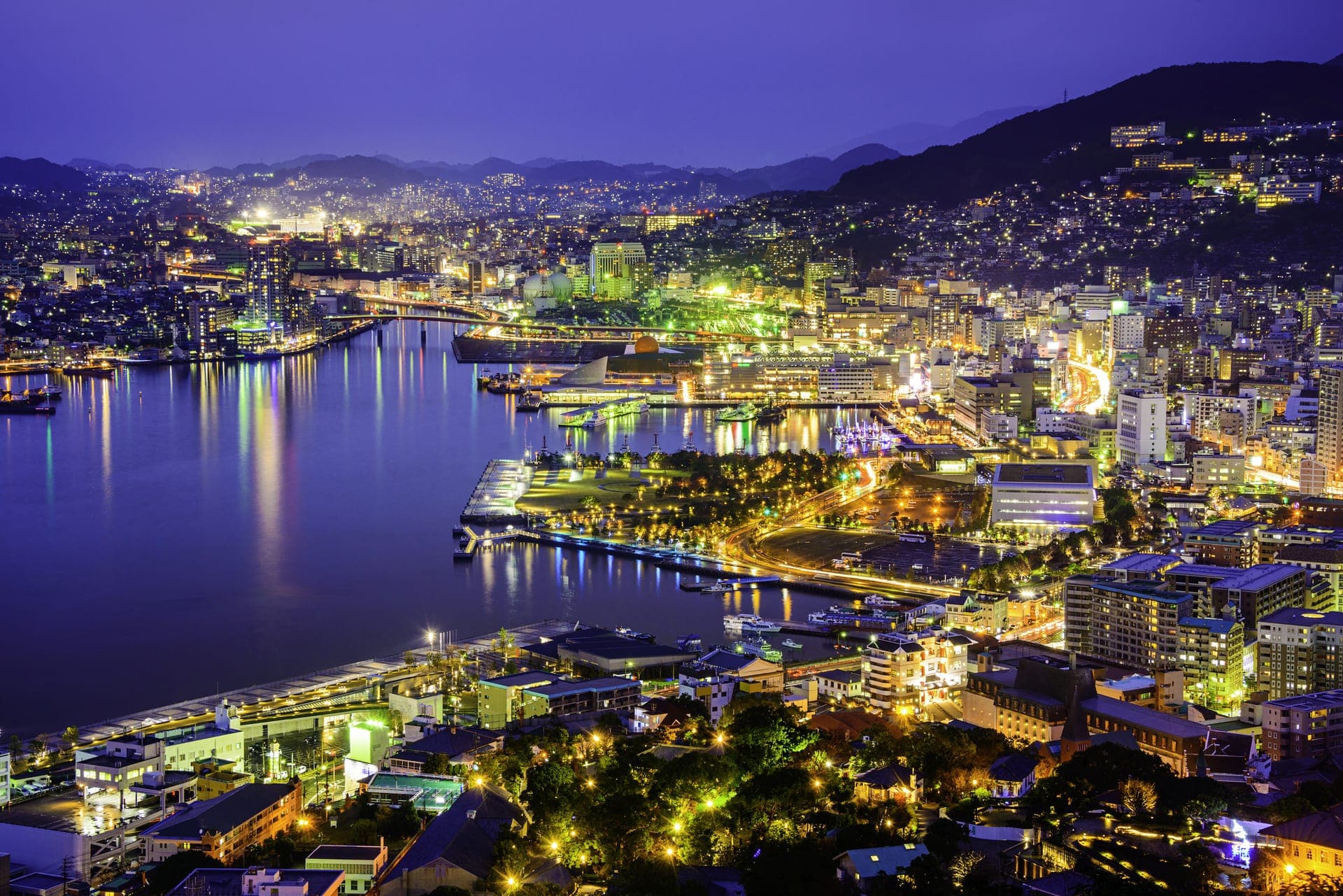 Nächtliches Panorama von Nagasaki – die beleuchtete Stadt zieht sich um die dunkle Hafenbucht und die Hügel hinauf