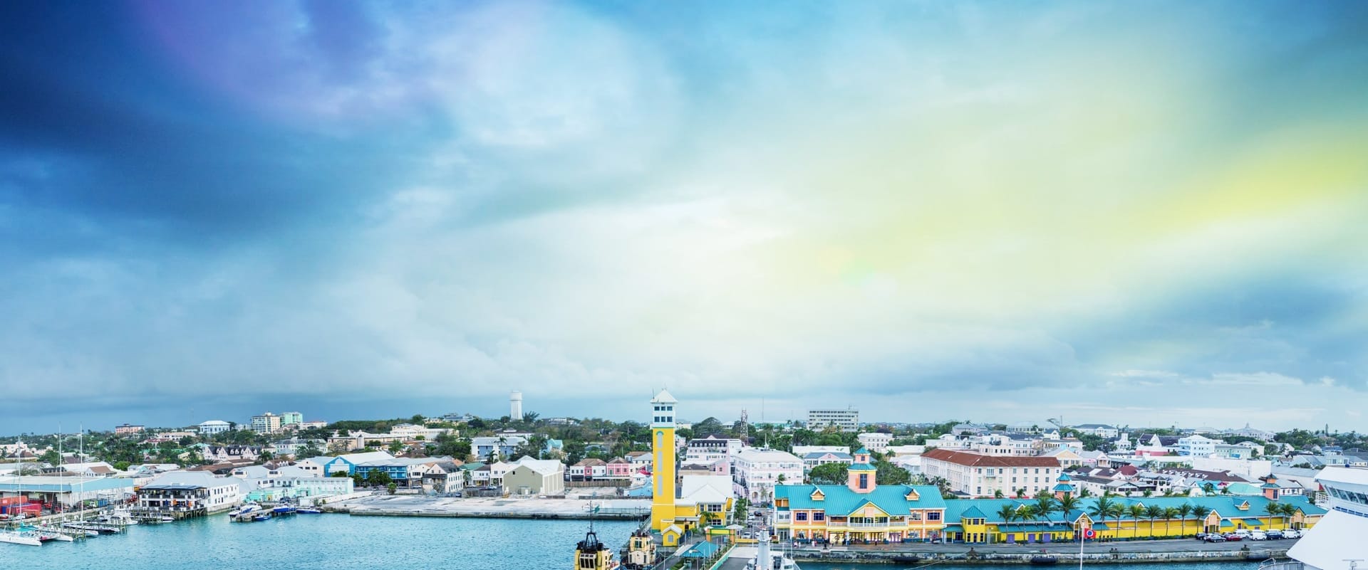 Panoramablick auf den Hafen von Nassau mit dem gelben Uhrenturm und bunten Häusern von Downtown bei Sonnenuntergang