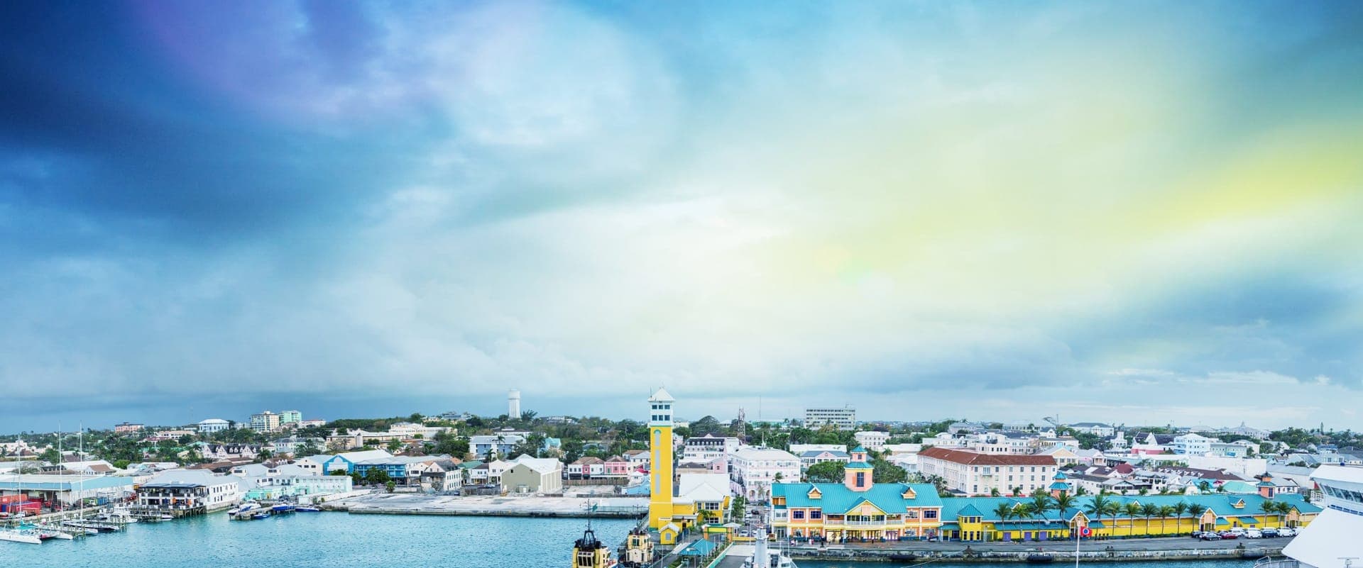 Panoramablick auf den Hafen von Nassau mit dem gelben Uhrenturm und bunten Häusern von Downtown bei Sonnenuntergang
