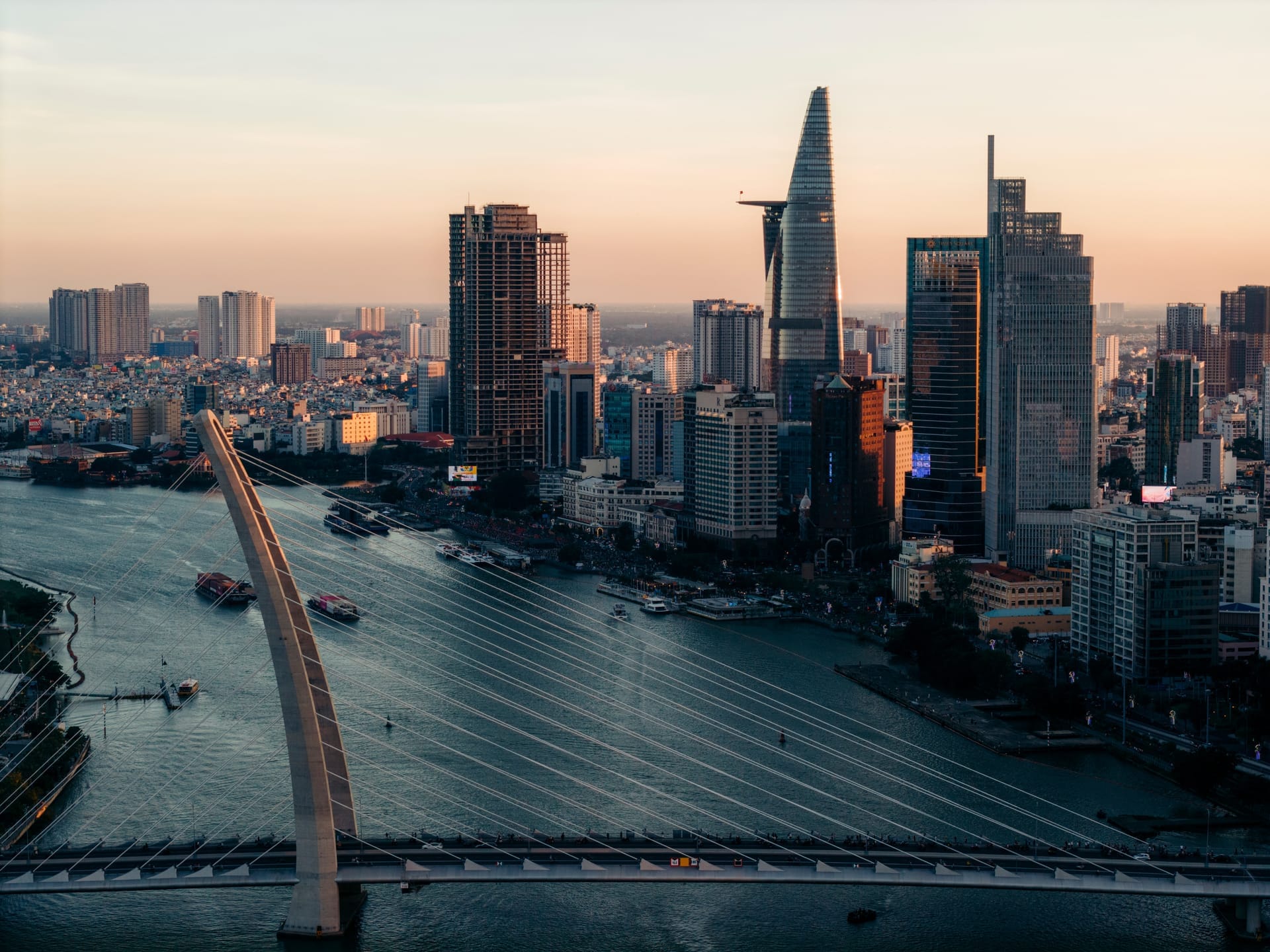 Skyline von Ho-Chi-Minh-Stadt bei Sonnenuntergang mit Hochhäusern am Fluss und Booten auf dem Wasser
