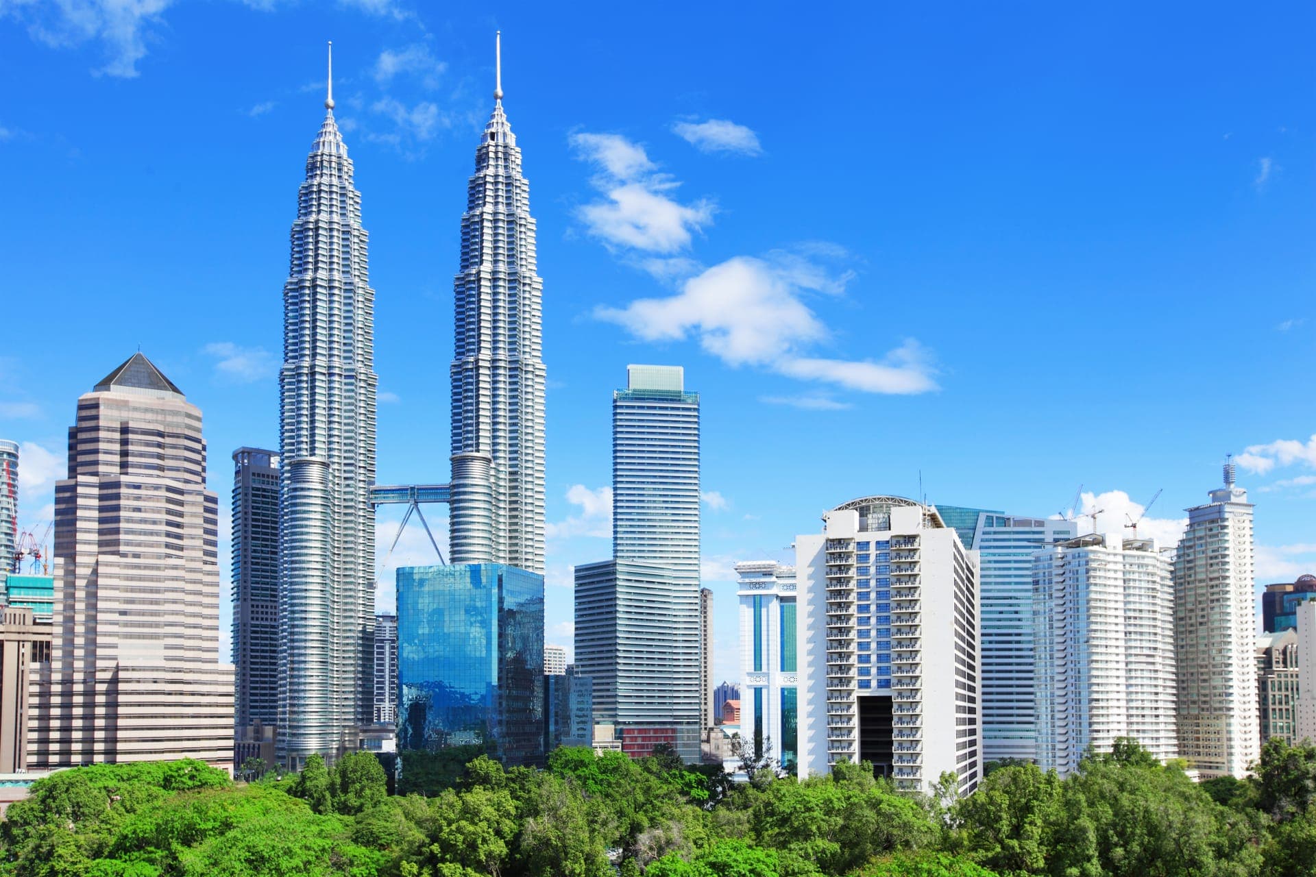 Skyline von Kuala Lumpur mit den Petronas Towers und umliegenden Hochhäusern über den Baumkronen des KLCC-Parks bei Tageslicht