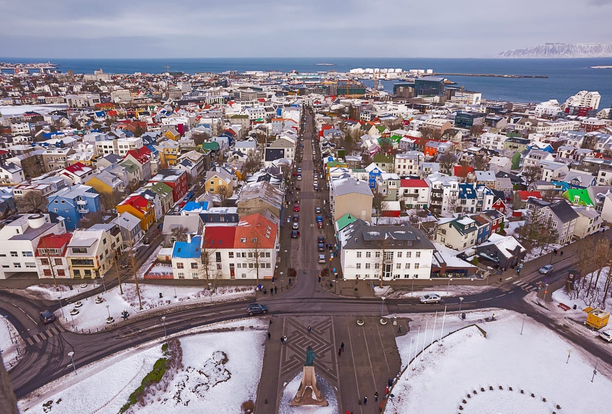 Blick vom Turm der Hallgrímskirkja über die bunten Blechdächer Reykjaviks bis zum Hafen und zum verschneiten Bergrücken auf der anderen Seite der Bucht