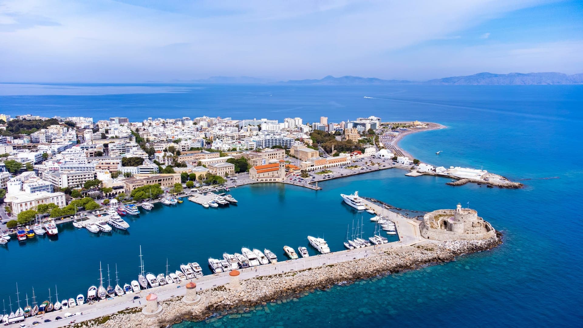 Blick über den Mandraki-Hafen von Rhodos mit Windmühlen und der mittelalterlichen Stadtmauer im Hintergrund