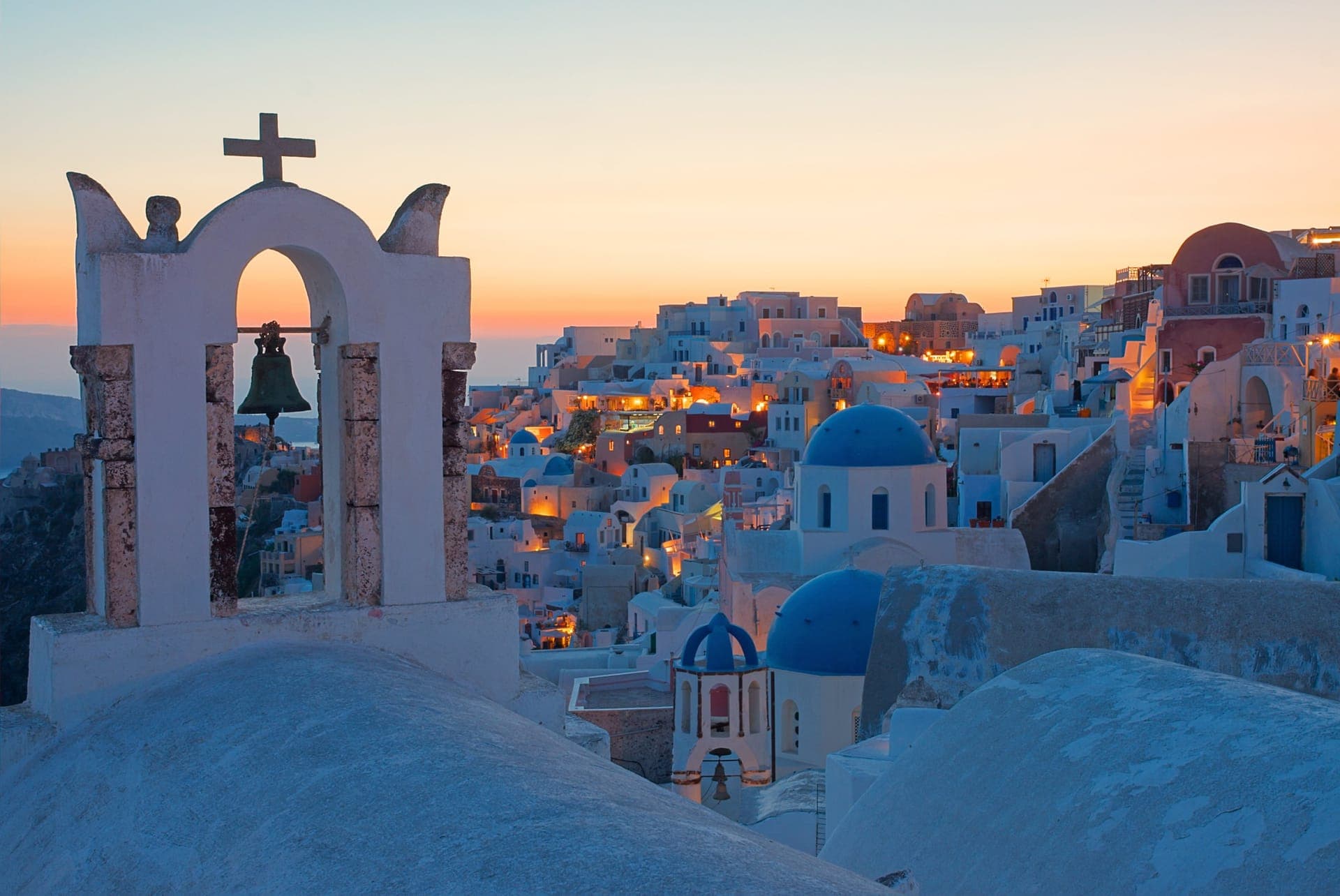 Oia auf Santorini in der blauen Stunde mit beleuchteten weißen Häusern, blauen Kirchenkuppeln und einem Glockenbogen im Vordergrund