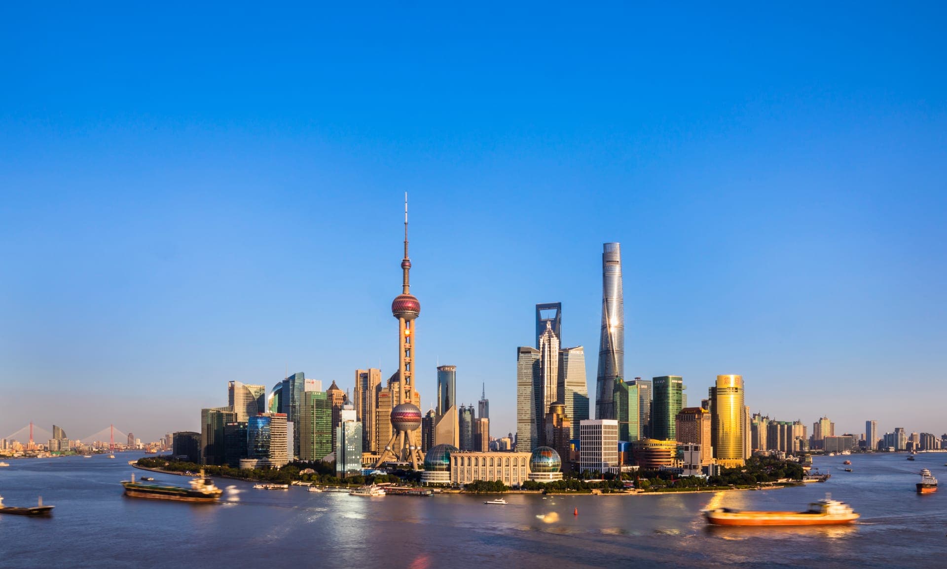 Die Skyline von Pudong mit dem Oriental Pearl Tower über dem Huangpu-Fluss, davor fahren Schiffe