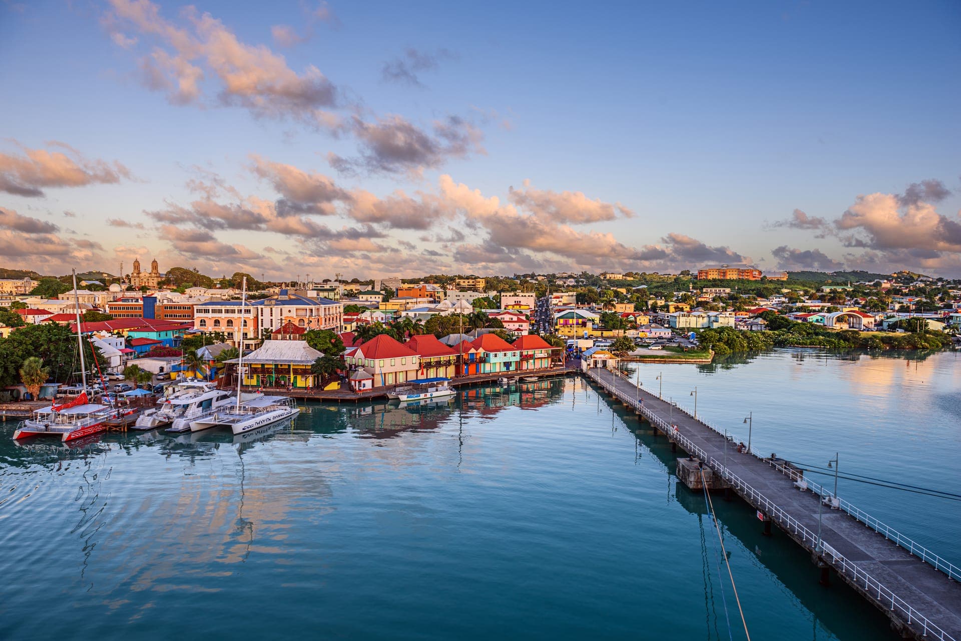 Blick vom Wasser über den Hafen von St. John's auf Antigua im Morgenlicht, mit Katamaranen, den bunten Dächern am Redcliffe Quay und den weißen Türmen der Kathedrale am Horizont