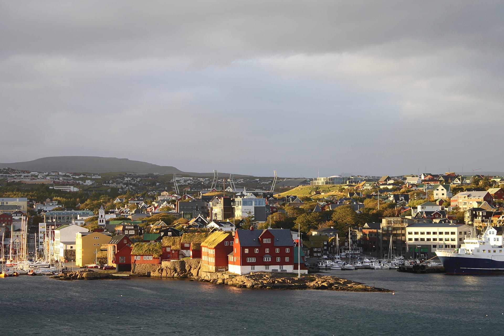 Die Halbinsel Tinganes in Tórshavn im Abendlicht, rote Holzhäuser mit Grasdächern über dem Wasser