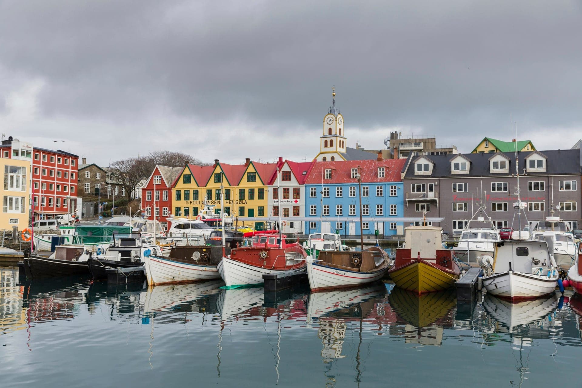 Bunte Häuser und Fischerboote im Hafen von Tórshavn auf den Färöern, im Hintergrund die Kirche mit Turmuhr