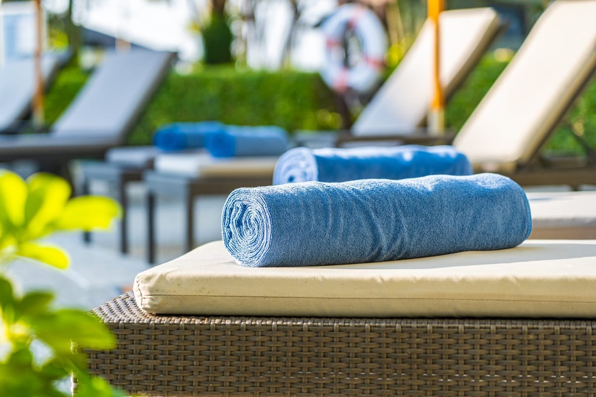 Zusammengerollte Handtücher liegen bereit auf Liegestühlen rund um einen Pool