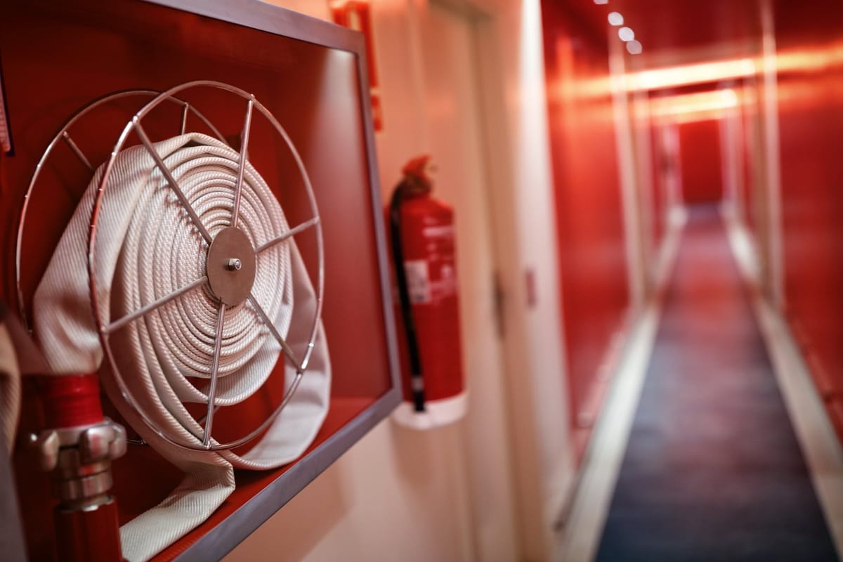 Aufgerollter Löschschlauch in einem roten Wandkasten und ein Feuerlöscher an der Wand eines schmalen Kabinengangs