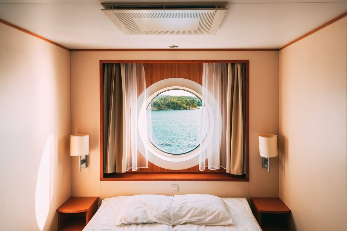 Blick durch das Bugfenster einer kompakten Schiffskabine mit Bett und Meerblick