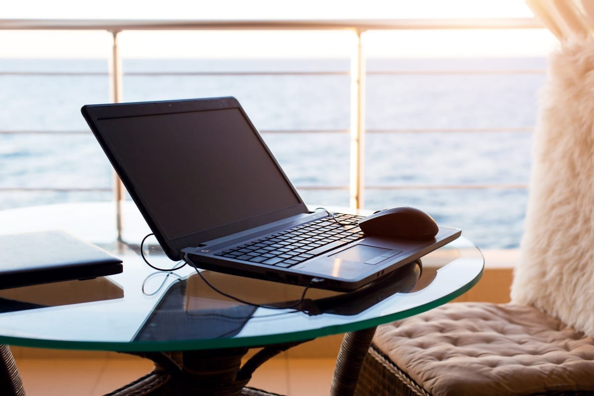 Aufgeklappter Laptop auf einem Tisch auf dem Kabinenbalkon mit Blick aufs Meer
