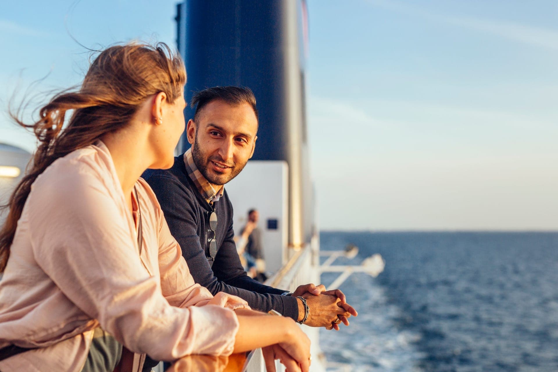 Paar blickt nachdenklich von der Reling eines Kreuzfahrtschiffs auf das Meer