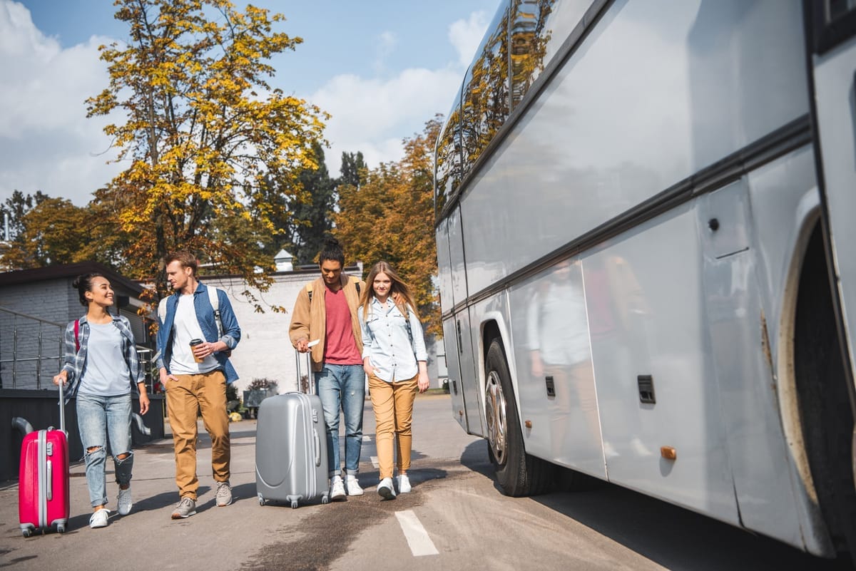Reisegruppe mit Rollkoffern geht auf einen wartenden Reisebus zu