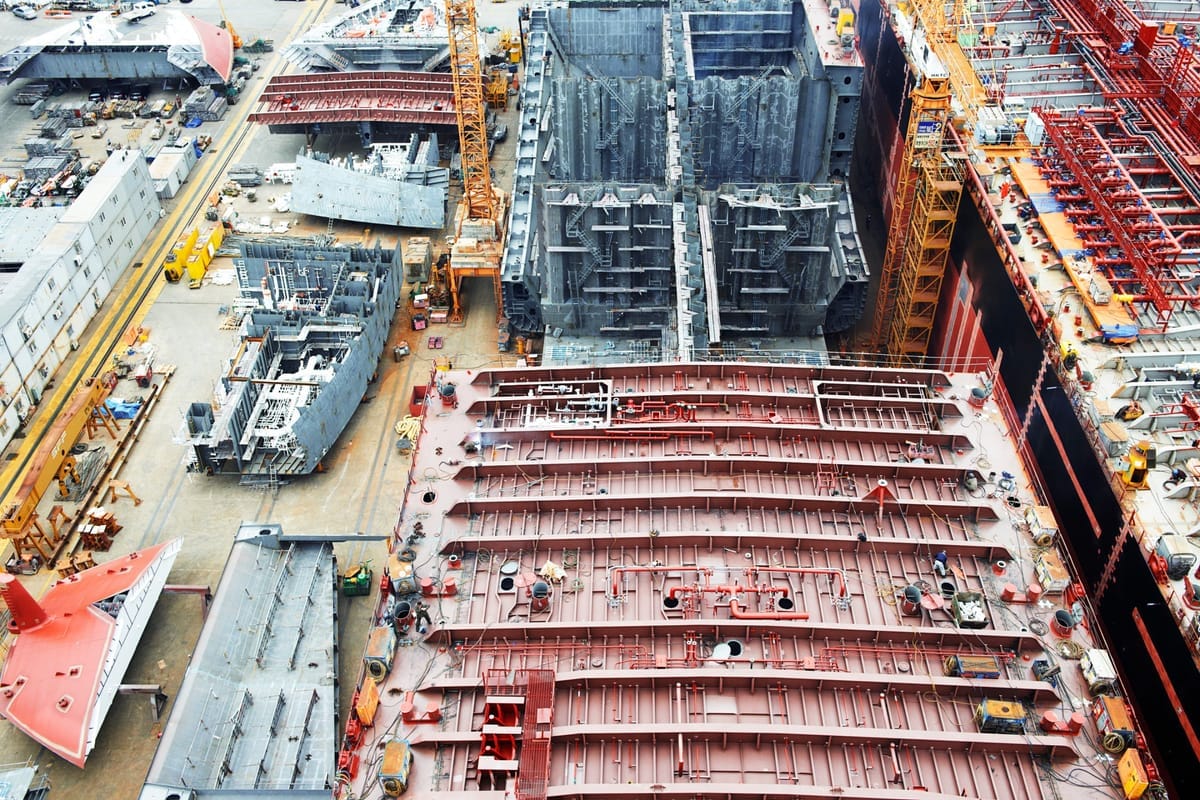 Luftaufnahme einer Werft mit dem Rumpf eines im Bau befindlichen Großschiffs zwischen Kränen