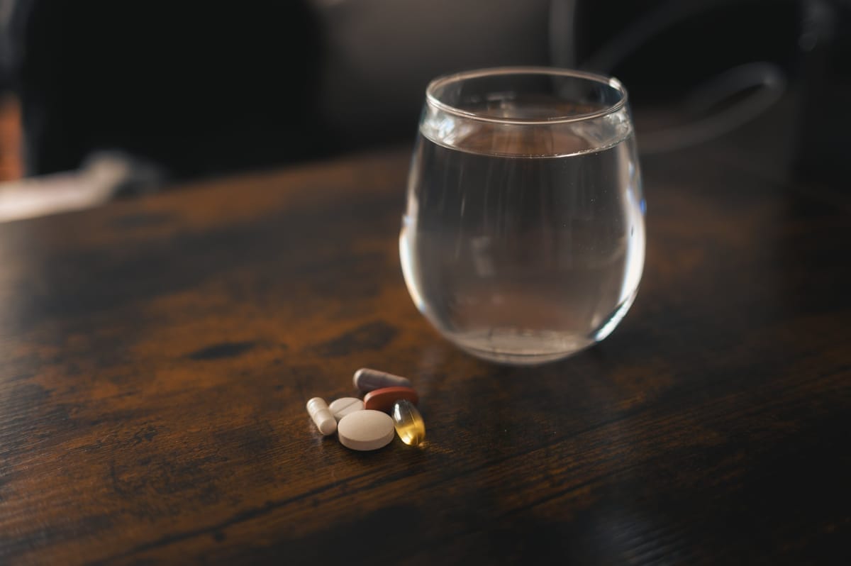 Tabletten und Kapseln gegen Reiseübelkeit neben einem Glas Wasser