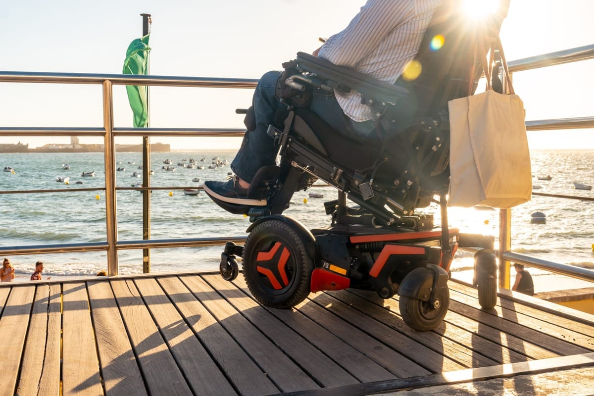 Person in einem Elektrorollstuhl auf einem hölzernen Pier mit Blick aufs Meer bei Sonnenuntergang