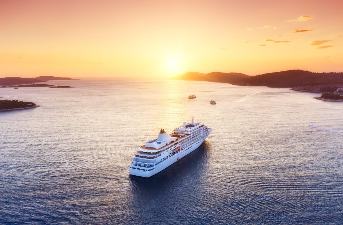 Kreuzfahrtschiff aus der Luft bei Sonnenuntergang zwischen Küstenlinien auf offenem Wasser
