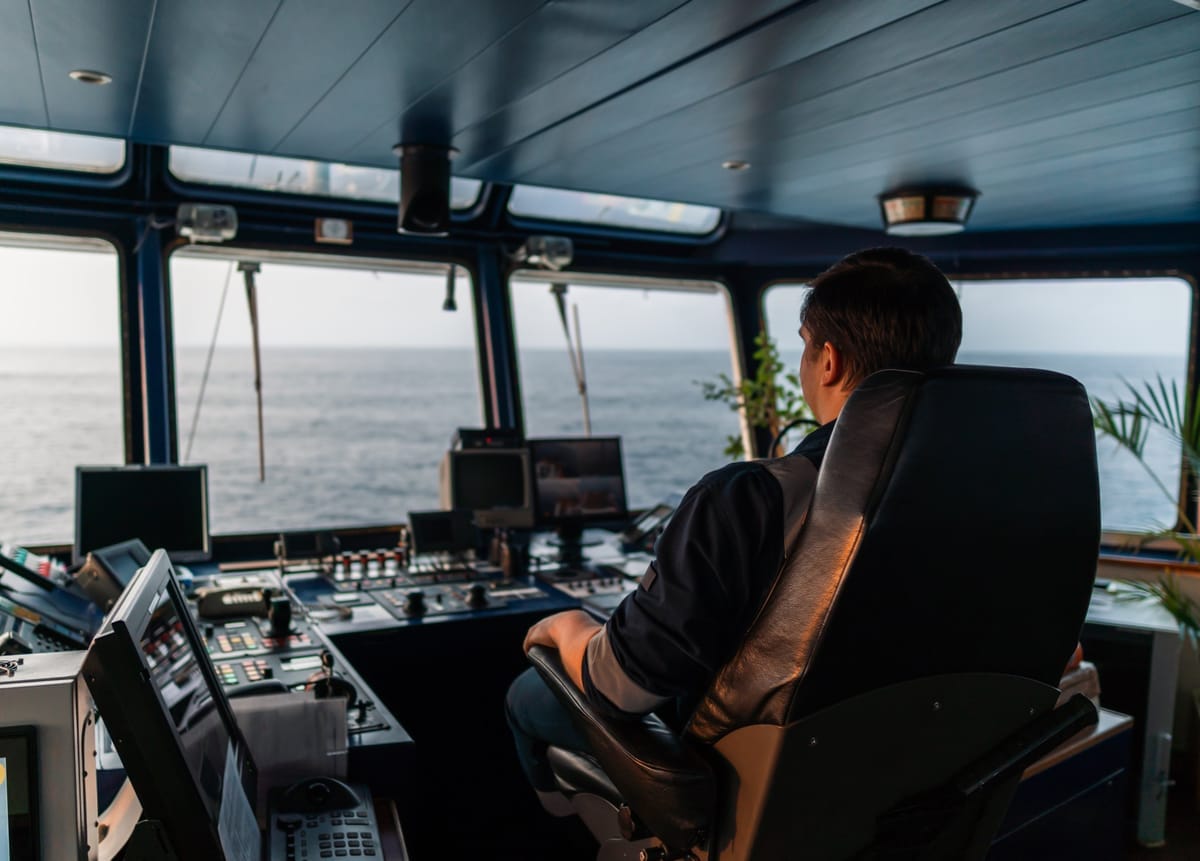 Nautischer Offizier sitzt auf der Kommandobrücke vor Radar- und Steuerkonsolen mit Blick aufs offene Meer