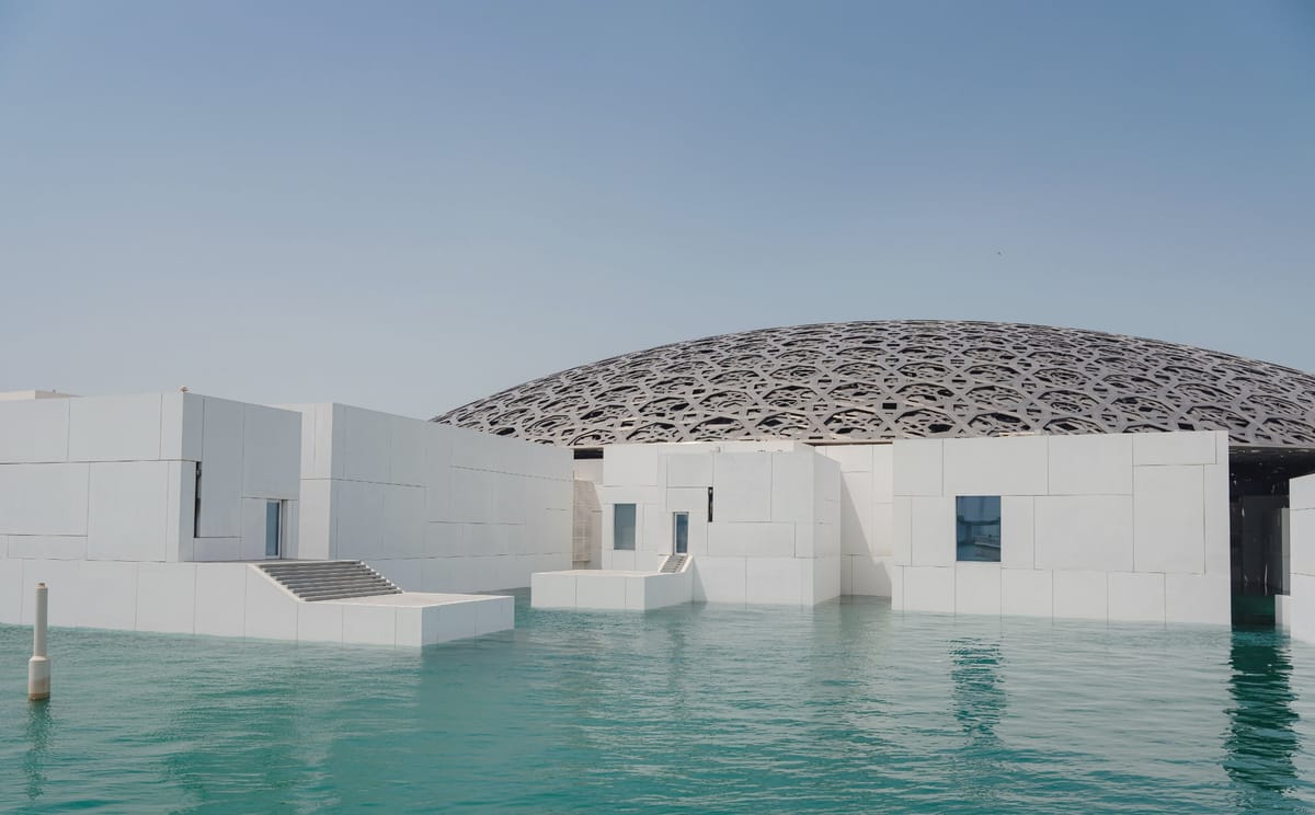 Die silberne Gitterkuppel des Louvre Abu Dhabi über dem Wasser