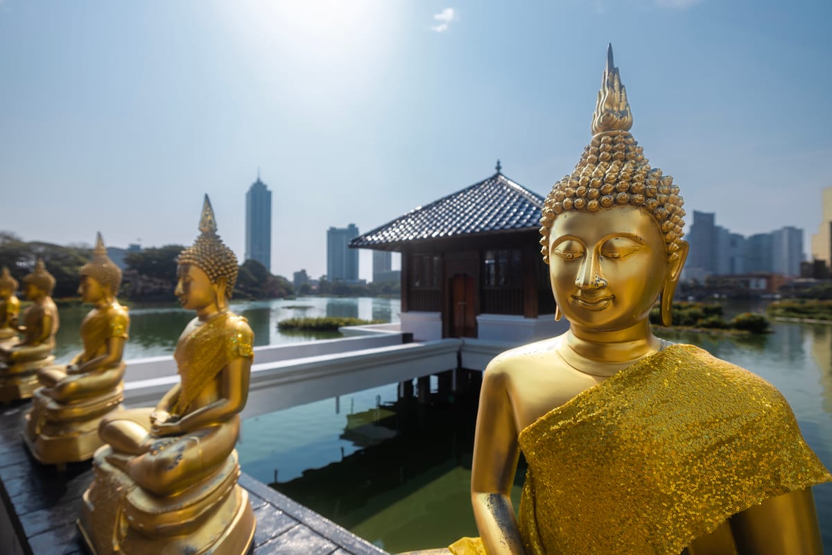 Reihe goldener Buddha-Figuren auf der Plattform des Seema-Malaka-Tempels im Beira-See, dahinter Wasser und Hochhäuser von Colombo