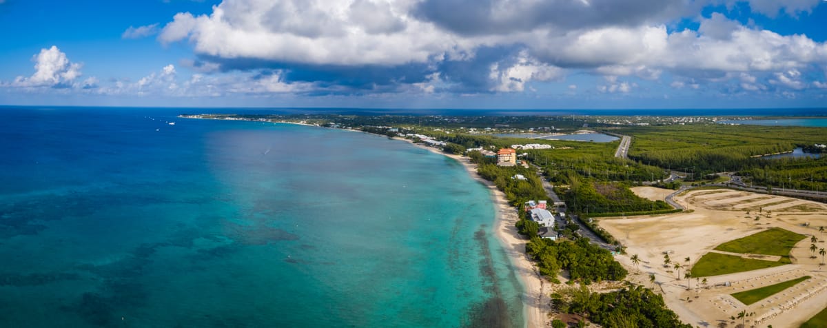 Luftbild des Seven Mile Beach auf Grand Cayman mit türkisfarbenem Wasser, hellem Sand und grünen Bäumen