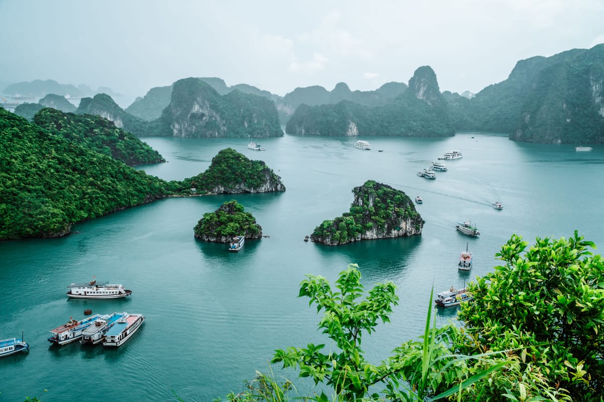 Blick von oben über die Karstinseln der Halong-Bucht mit mehreren Ausflugsbooten auf dem türkisfarbenen Wasser