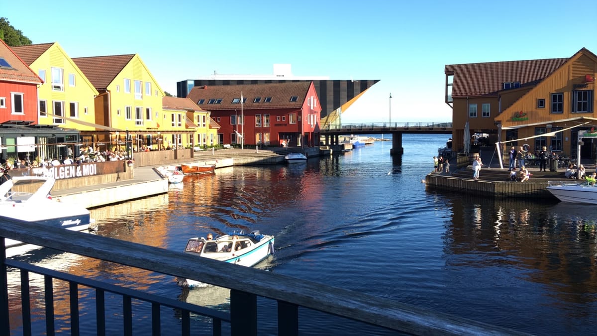 Bunte Holzhäuser und Restaurantterrassen am Kanal der Fiskebrygga in Kristiansand, davor Motorboote