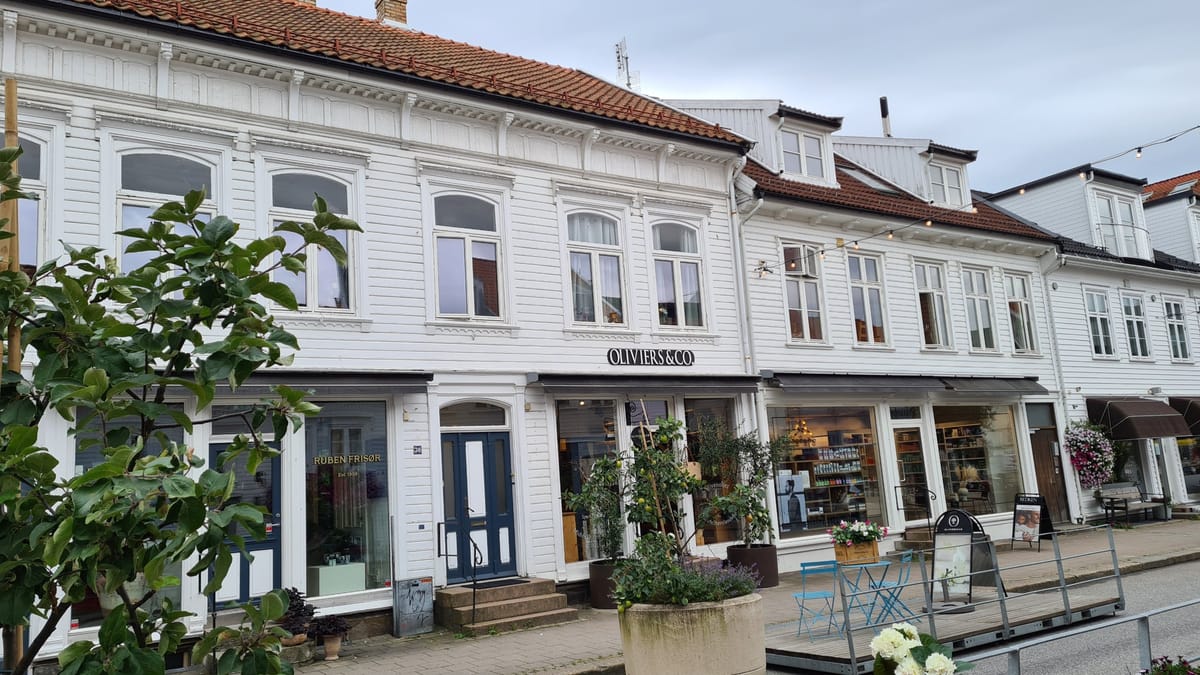 Weiß gestrichene Holzhäuser mit Sprossenfenstern und Läden im Erdgeschoss an einer Straße in Kristiansand