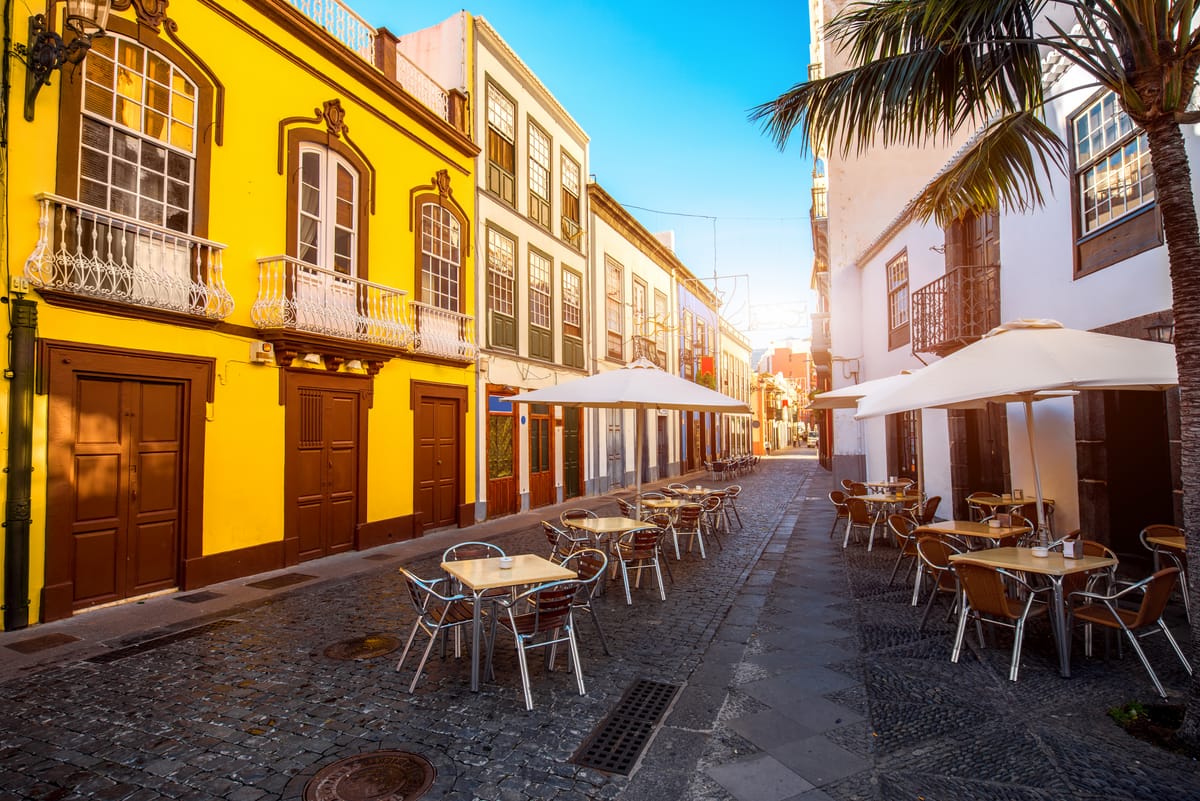 Kopfsteingepflasterte Gasse in Santa Cruz de La Palma mit gelben und weißen Häusern und Tischen vor den Lokalen