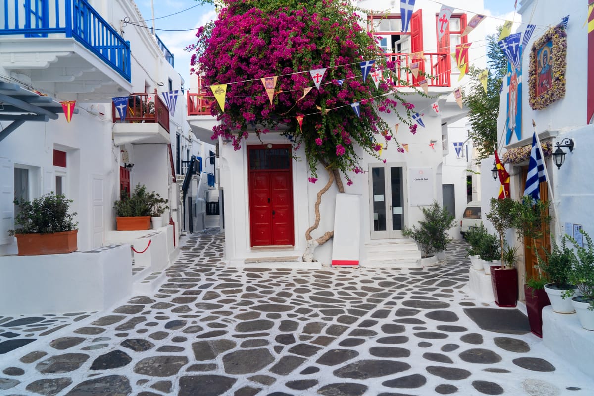 Enge weiße Gasse in der Chora von Mykonos mit blauen Türen und Bougainvillea