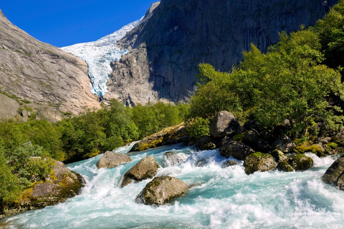 Gletscherzunge des Briksdalsbreen mit blauem Eis über dem milchig-grünen Gletschersee, Wanderweg im Vordergrund
