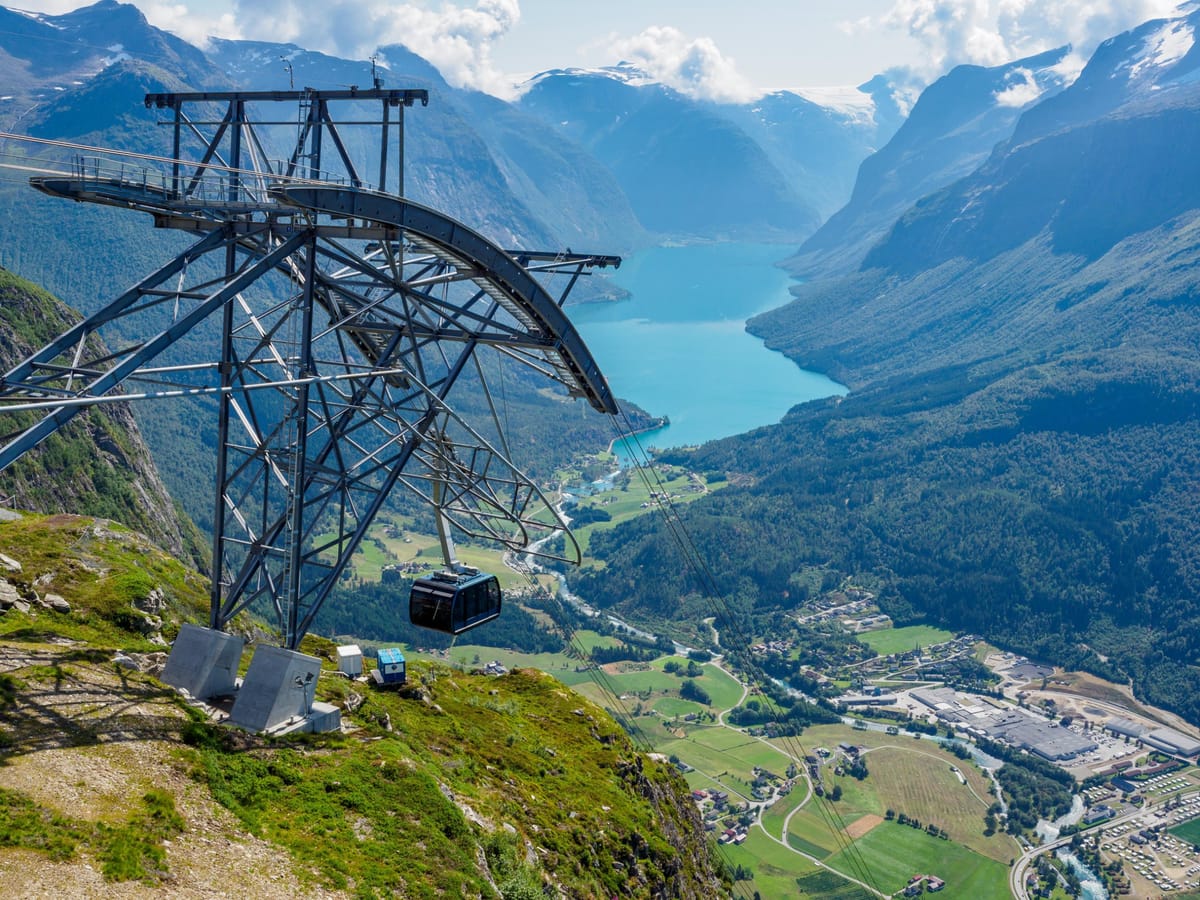 Eine Gondel des Loen Skylift hängt an der Bergstation auf dem Hoven, tief darunter liegen der türkisfarbene Lovatnet, das Tal von Loen und schneebedeckte Gipfel