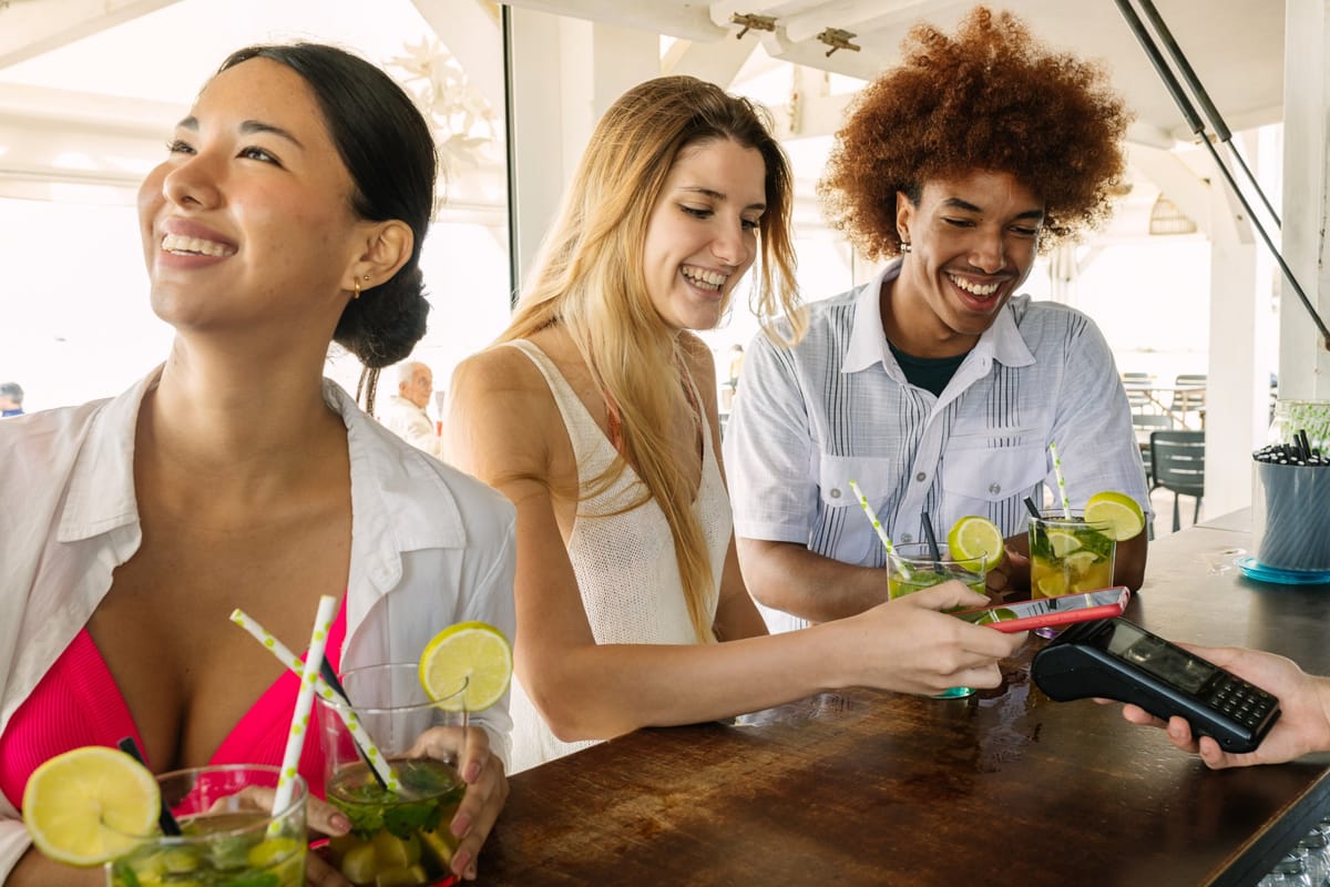 Junge Frau bezahlt an einer Bartheke Cocktails kontaktlos mit einer Karte am Kartenlesegerät
